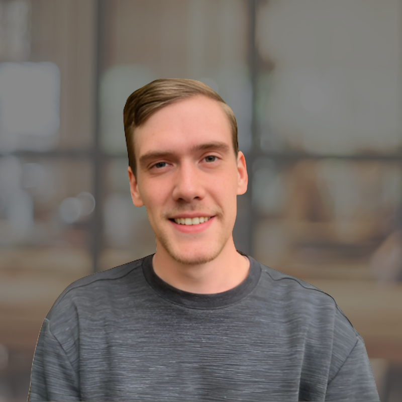 Headshot of Wyatt smiling, wearing a gray shirt against a blurred indoor background.