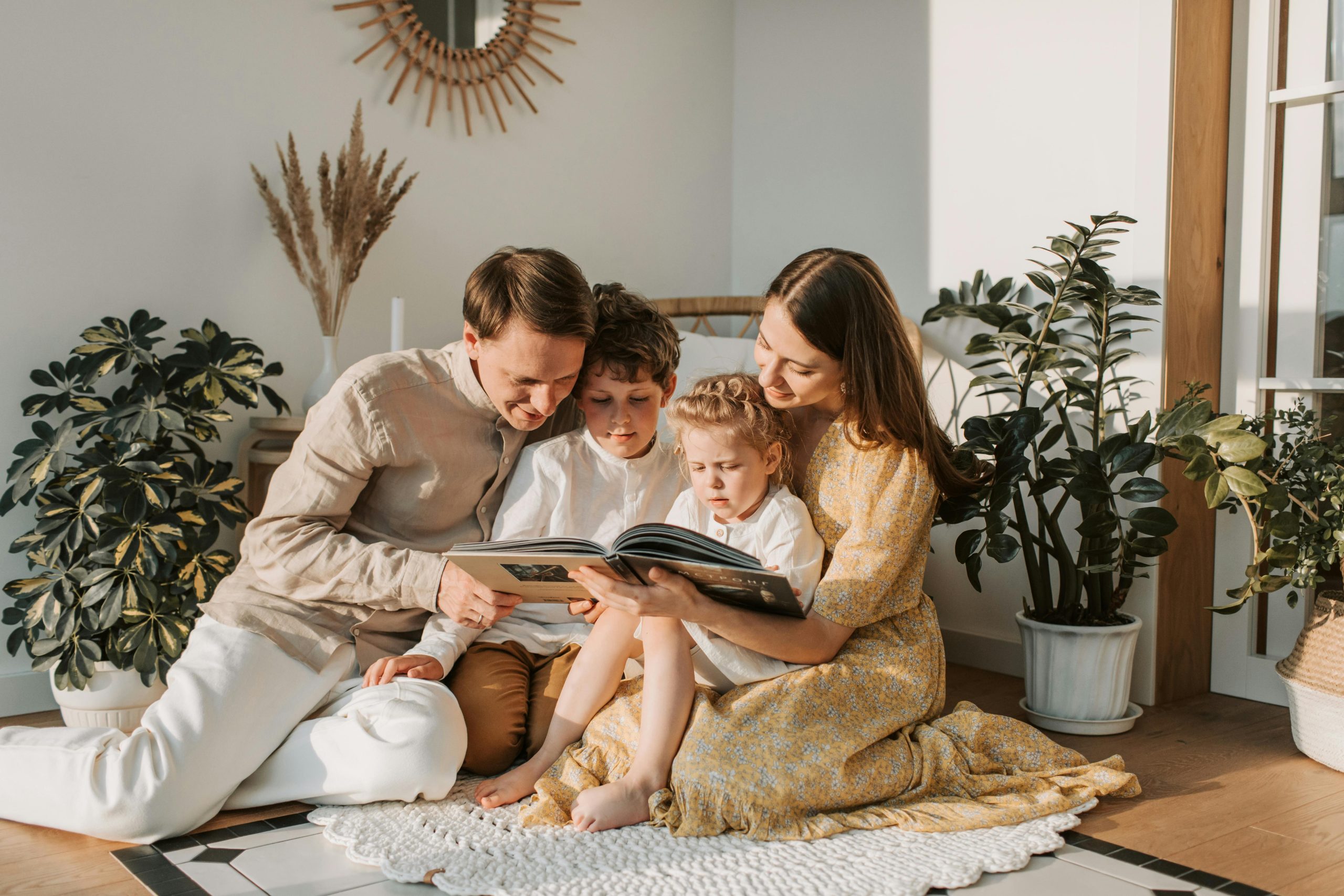 Parents and two young children reading a book together at home in a cozy living room.